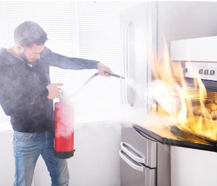 Man putting out kitchen fire with a fire extinguisher.